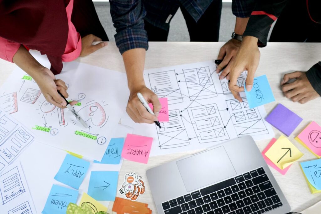 People with markers working on website blueprints on a white table.